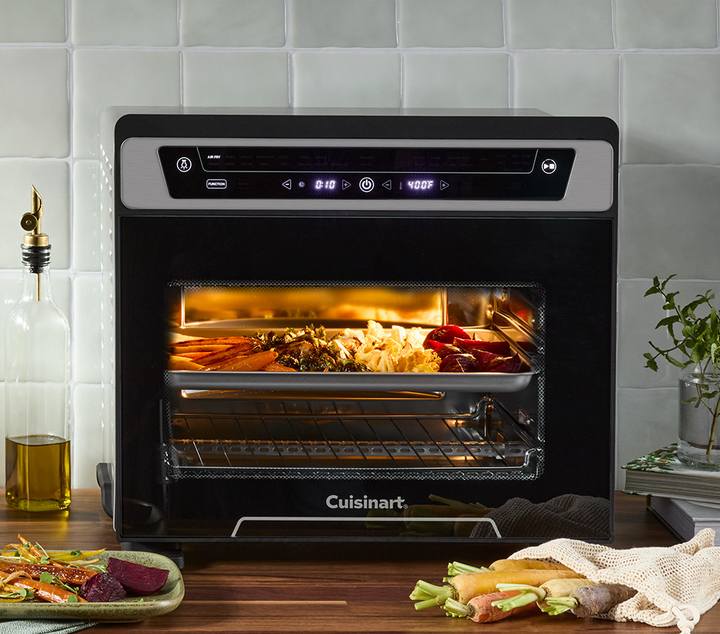 Toaster oven with light on, lots of veggies and a delicious fall meal cooking inside